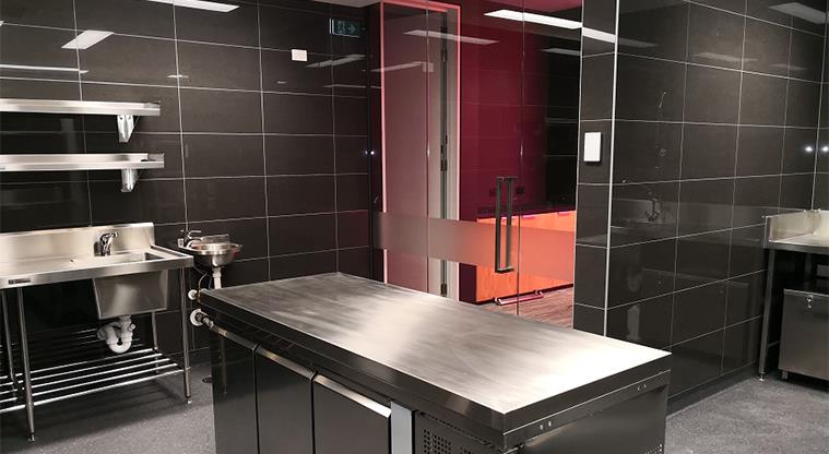 A kitchen with sleek black tiles and stainless steel benchtops and facilities.