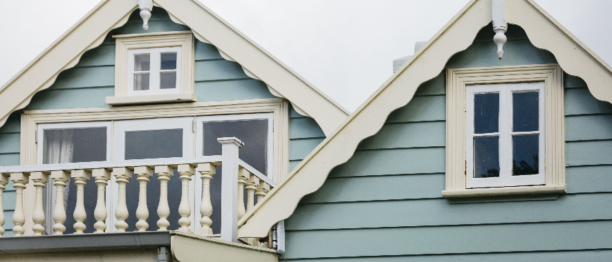 Close up of the front facade of an old villa with light blue weatherboards and light yellow window trims.
