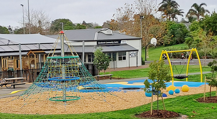 Crossfield Reserve - Playground with a net climbing frame, a basket swing and in-ground trampolines with the Glendowie Community Centre in the background.