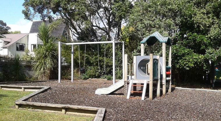 Herald Island Domain - Playground with climbing equipment and swings on a bark base.