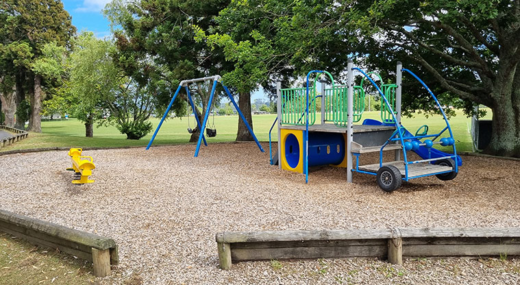 Huapai Recreation Reserve - Climbing frame in the shape of a car with tunnel, spinning balls, steering wheels and tyres, and a rocker toy and swing set.