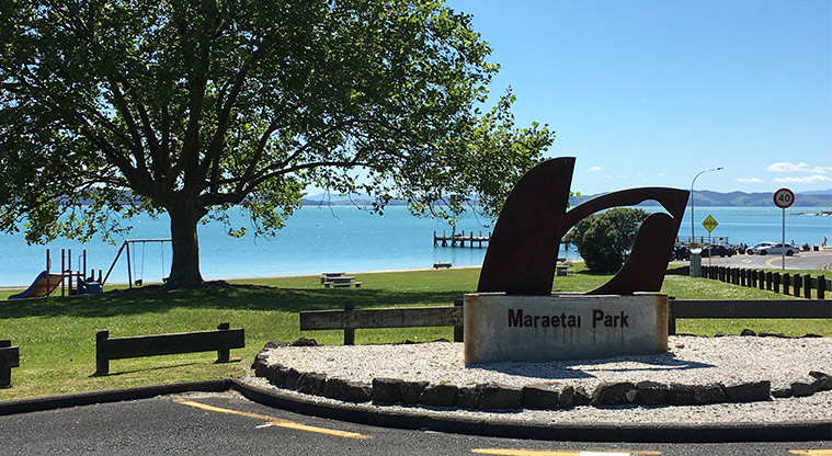Maraetai Park - Sign at the entrance to the park and car park with the preschool playground and beach in the background. Photo credit: S Hulse.