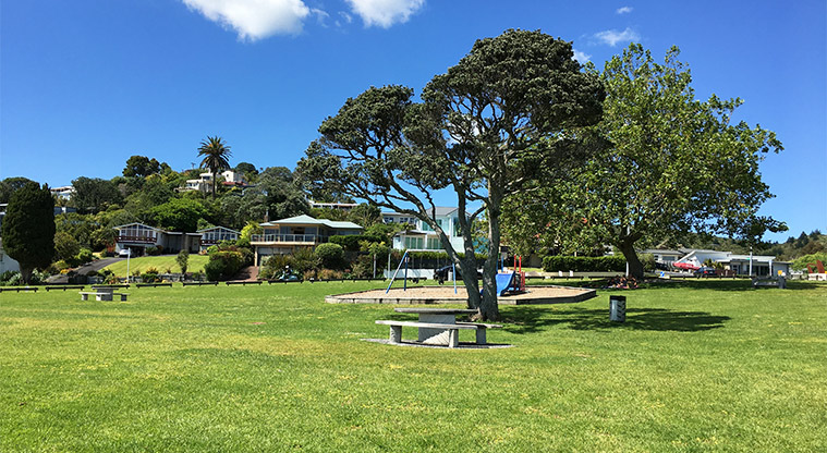 Maraetai Park - Open space with the preschool playground and large trees in the background. Photo credit: S Hulse.