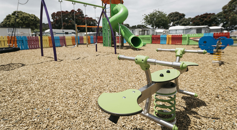 Martins Bay Holiday Park - Playground with rocker toys, swings, climbing tower and slide, and colourful picket fence in the background.