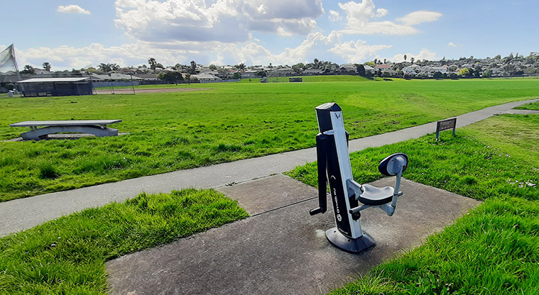 Meadowlland Park - One of the pieces of fitness equipment with a seat, open space and softball diamond in the background.