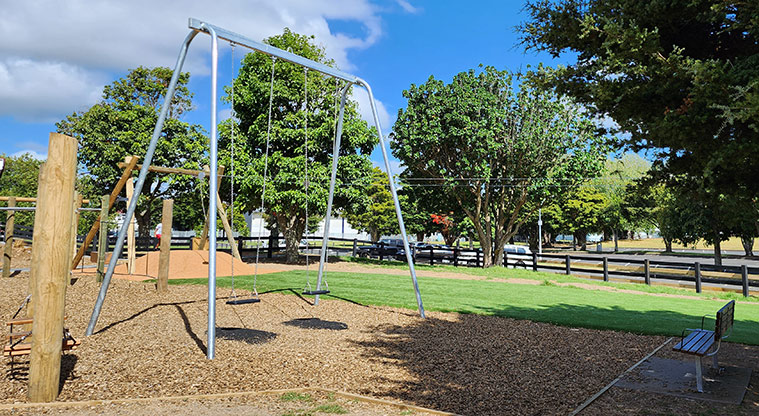 Ngāti Ōtara Park - Set of two swings with a nearby seat and trees.