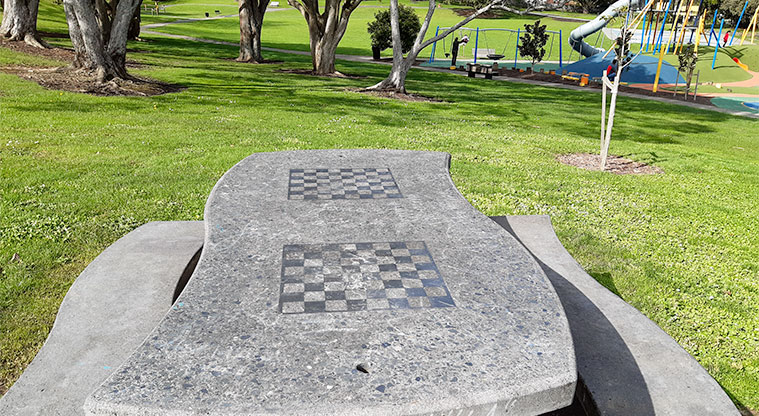 Potters Park - Picnic table with chess board inlaid, playground and trees in the background.