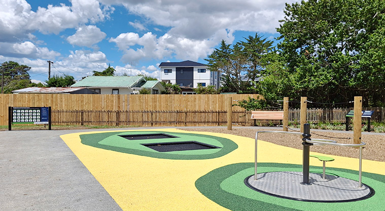 Rānui Domain - Inclusive seated spinner with the in-ground trampolines and communication board in the background.