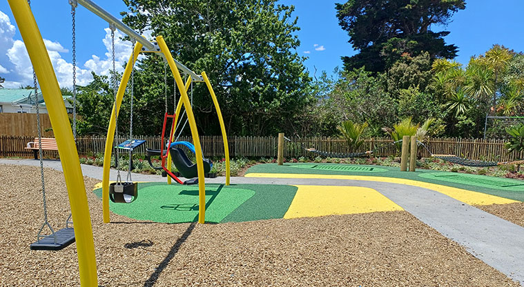 Rānui Domain - Section of the swing set with a flat path and hammocks in the background.