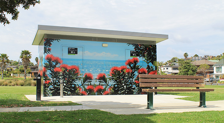 Red Beach Park - Toilets with a pōhutukawa mural, and a park bench in the foreground. Photo credit: M Loubser.