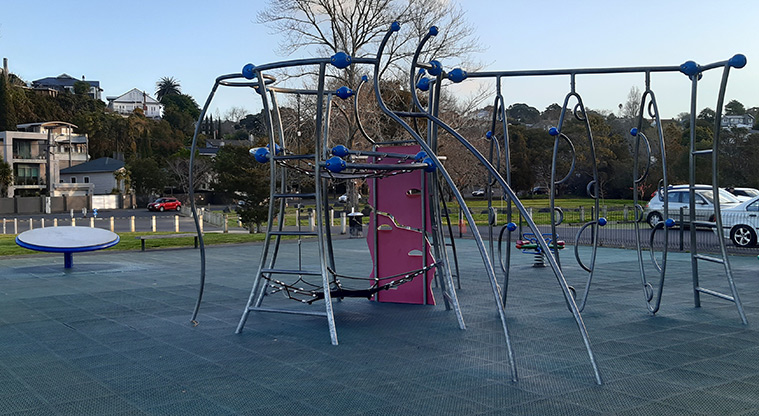 Shore Road Reserve - Play structure with climbing wall, net ropes, and ladders, and a round spinning platform in the background.