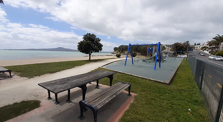 St Heliers Bay Beach Reserve - Picnic table and playground with the beach and Rangitoto Island in the background.