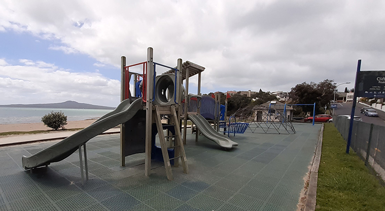 St Heliers Bay Beach Reserve - Play module with ladder, climbing wall and slide, with the rest of the playground and toilets in the background.