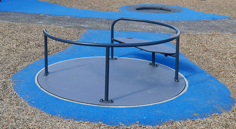 Taipari Strand - Carousel on a blue rubber surface, with an in-ground trampoline in the background.