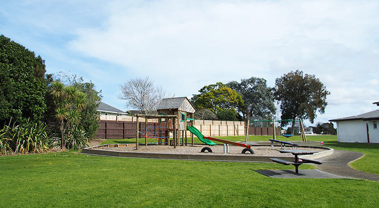 Te Atatū Peninsula Park - The playground on a bark base with the path on the right and a picnic table in the foreground.