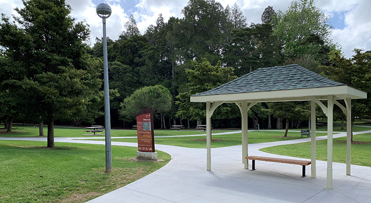 Tōtara Park - Roofed shelter at the intersection of a number of paths, with open space and trees in the background.