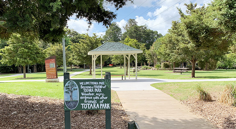 Tōtara Park - Friends of Tōtara Park sign with the shelter, paths and trees in the background.