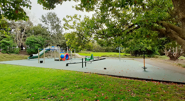 Waiatarua Reserve - Open grrassed area and the playground surrounded by established trees.