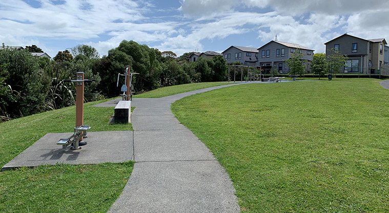 Waimāhia-ki-uta / Waimahia Park - Open grassed space with fitness equipment alongside the footpath.